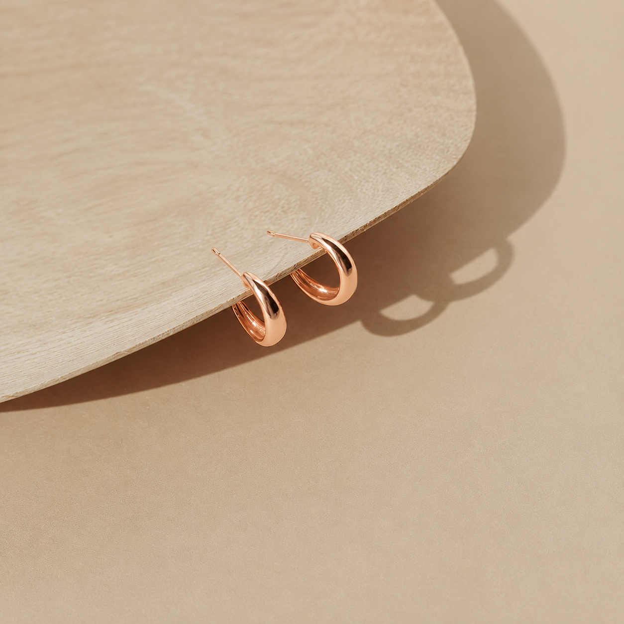 Rose gold hoop earrings on a beige stone surface